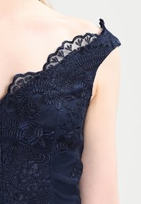 Navy blue dress with floral lace embroidery, v-neck design, and scalloped edges on the shoulder, featuring smooth satin texture.