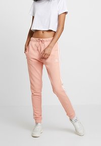 Ljust rosa joggerbyxor med dragsko i midjan, vita sidostripes, ribbade mudd och en broderad logotyp på vänster lår.