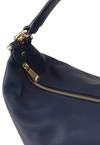 Marine leren tas met een gebogen vorm, voorzien van een gouden rits en hardware. Gladde textuur met zichtbare stiksels en een enkele schouderriem.