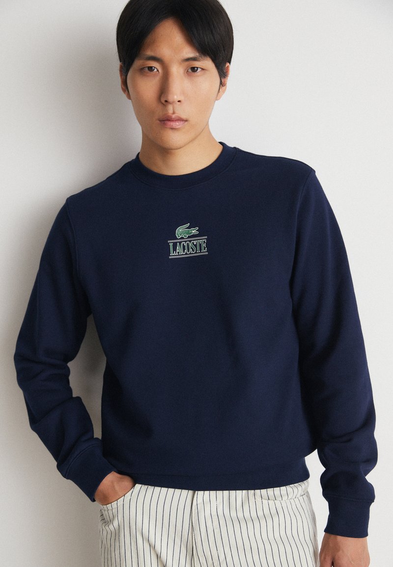 Granatowy sweatshirt z miękkiej tkaniny, z prążkowanymi mankietami i dekoltem, z wyhaftowanym na piersi zielonym logo Lacoste.