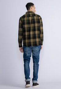 Schwarz-olivgrün karierte Flanellhemd mit einem taillierten Kragen, geknöpften Manschetten und einem abgerundeten Saum, kombiniert mit blauen Jeans und schwarzen Stiefeln.