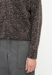 Sweatshirt com estampa de leopardo em tons de castanho e preto, apresentando um bolso canguru e punhos canelados, combinado com calças cargo cinzas.