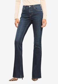 Donkerblauwe flare jeans met een middelhoge tailleband, voorzien van voorzakken, een knoopsluiting en contrasterende stikdetails.