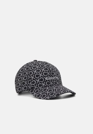 Casquette de baseball noire couverte de lettres blanches "CK" répétées avec le logo "Calvin Klein" au centre à l'avant, présentée sur un fond clair.
