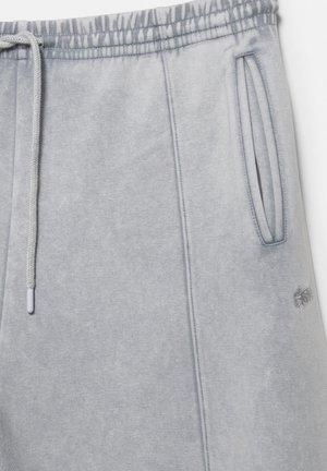 Jasnoszare spodnie dresowe z elastycznym pasem, sznurkiem, bocznymi kieszeniami i subtelnym haftowanym logo w pobliżu kieszeni.
