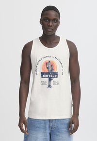 Balts kokvilnas topiņš bez piedurknēm ar krāsainu kaktusa un saules grafiku, uzdrukāts zilā un oranžā krāsā ar tekstu par moteļiem. Ikdienišķa piegriezuma.