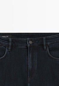 Jeans in denim blu scuro con un classico design a cinque tasche, chiusura con bottone e cuciture a contrasto lungo le cuciture.