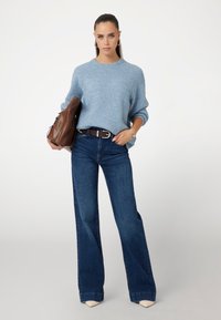 Maglione lavorato a maglia azzurro chiaro con maniche raglan, jeans a zampa d'elefante blu scuro, borsa in pelle marrone e tacchi a punta color crema.