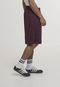 Shorts de sport bordeaux à rayures verticales, taille élastique, poches latérales ; assortis à des baskets bleu marine et des chaussettes blanches avec des rayures noires.