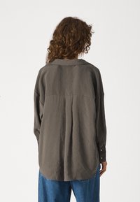 Camicia a maniche lunghe, dalla vestibilità ampia, in tessuto grigio scuro, con yoke posteriore e dettagli delle cuciture, con polsino abbottonato e orlo arrotondato.