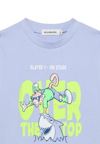 Γαλάζιο βαμβακερό t-shirt με στρογγυλή λαιμόκοψη, που απεικονίζει γραφικό σχέδιο ενός πιθήκου με γυαλιά ηλίου και νέον πράσινο κείμενο: «ΠΑΙΚΤΗΣ 1 - ΣΤΗ ΣΚΗΝΗ ΠΑΝΩ ΑΠΟ ΤΑ ΟΡΙΑ.»