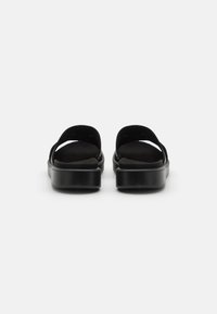 Zwarte slipper sandalen met een zachte suede bovenkant, open ontwerp en een glanzende platformzool. Minimalistische stijl met een gebogen, comfortabele vorm.