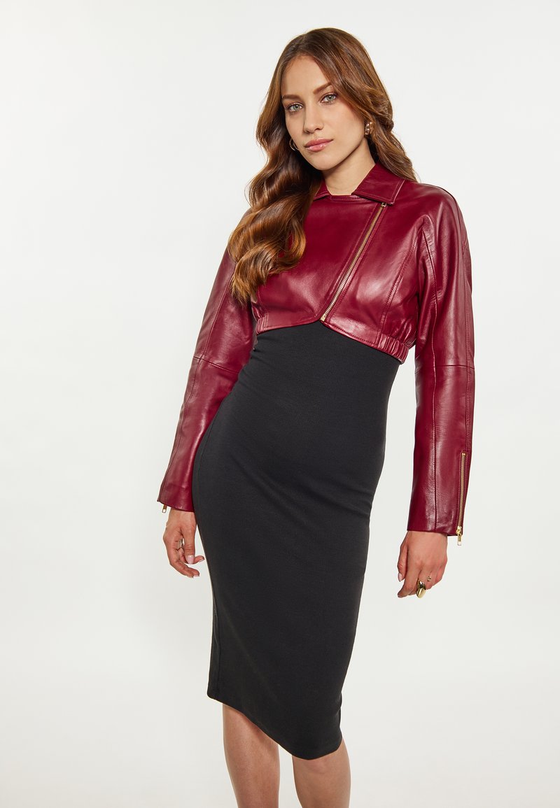 Giacca cropped in pelle rossa con zip asimmetrica, abbinata a un vestito midi nero aderente. Texture liscia, design sartoriale e silhouette moderna.