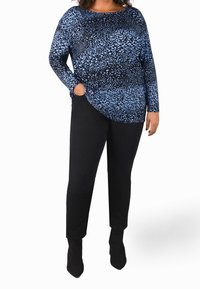 Blau gemustertes Langarmshirt mit Rundhalsausschnitt und Taschen, kombiniert mit schwarzen Slim-Fit-Hosen und Ankle-Boots.