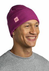 Purple ribbed beanie with a pink Buff logo patch, soft texture, and snug fit. Worn by a person in a gray sweater, showcasing its design.