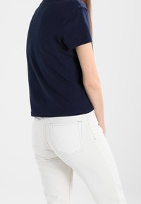 Navyblaue Baumwoll-T-Shirt mit Rundhalsausschnitt und kurzen Ärmeln, kombiniert mit weißen Jeans, die über Gesäßtaschen und eine körpernahe Passform verfügen.