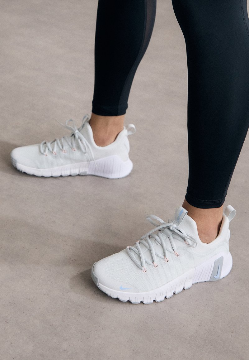 Scarpe da atletica grigie chiare con una tomaia texturizzata, dotate di lacci elastici e di una suola bianca spessa con scanalature texturizzate per una migliore trazione.