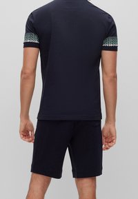 T-shirt bleu marine à manches courtes avec des accents de logo imprimés sur les manches, associé à un short bleu marine assorti, fabriqué en tissu léger et lisse.