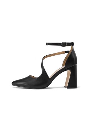 Scarpa con tacco alto in pelle nera, punta appuntita, cinturino alla caviglia con fibbia e tacco a blocco curvo su sfondo bianco.