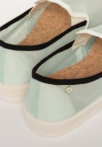 Baskets légères en mesh vert menthe avec des accents noirs, semelle intérieure en liège et un détail logo en forme de diamant doré. Présente une semelle blanche lisse.