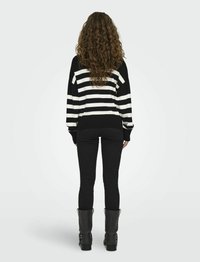 Zwart-wit gestreepte trui met een relaxed fit, gecombineerd met zwarte skinny jeans en kniehoge zwarte laarzen met hak, gezien van achteren.