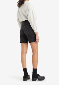 Svarta denimshorts med fransad nederkant, matchade med en grå långärmad topp och svarta ankelsockor, bärs med grova svarta träskor.