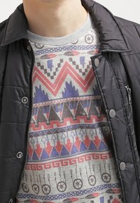 Chaqueta negra acolchada sobre un suéter gris con un patrón que presenta diseños geométricos en rojo, azul y negro. Tejido texturizado con un escote de tipo crew.