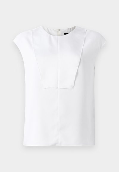 Hvit kortermet bluse med rund hals og rektangulært frontpaneldetalj, vist på en ensfarget bakgrunn.
