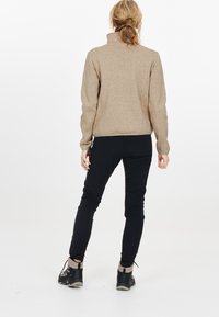 Tan fleecepullov med hög krage, tillsammans med svarta slim-fit byxor och svarta utomhusskor med grå detaljer.