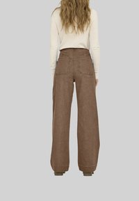 Un pantalon large marron avec une finition texturée, doté de deux poches arrière et de coutures visibles. Accompagné d'un pull léger.
