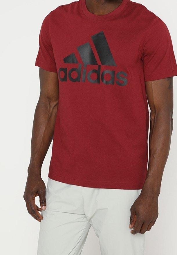 Punainen puuvillatee paidat, jossa on musta adidas-logo ja kolme raitaa etuosassa. Lyhyet hihat ja pyöreä kaula-aukko.