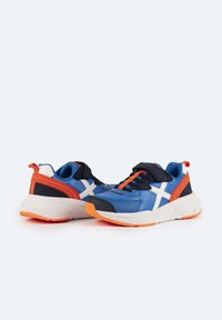 Baskets bleues et navy avec des accents blancs, des détails orangés, une sangle velcro et une tige en tissu texturé. Semelle blanche épaisse avec une semelle extérieure orange.