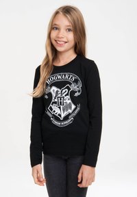 Schwarzes Langarmshirt mit einem weißen Hogwarts-Wappen-Design, das komplexe Details wie Tiere und Texte enthält. Aus weichem Baumwollstoff.