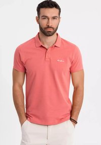 Polo tričko s krátkým rukávem v korálové barvě, vyrobené z měkké bavlněné tkaniny s klasickým límcem, s jemně vyšitým logo na hrudi.