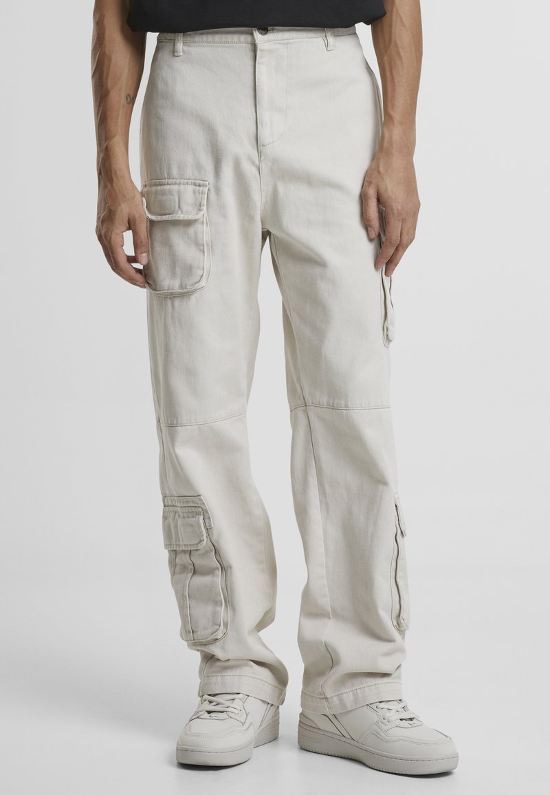 Beiga cargo-byxor med flera sidofickor, rak passform och tillverkade av bomull. Bärs med vita sneakers.