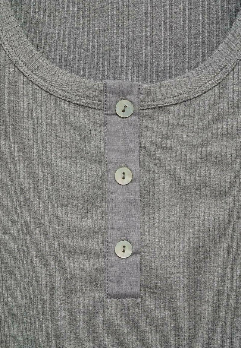 Primo piano del colletto di una camicia grigia a coste con tre bottoni rotondi allineati verticalmente su una pattina.