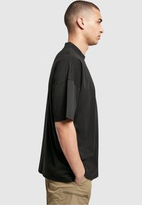 T-shirt noir à manches courtes avec col montant, coupe décontractée et texture lisse, associé à un pantalon cargo beige.