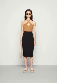 Top castanho com decote halter e recorte frontal, saia lápis preta, sandálias bejes e uma mala beige clara. Textura suave e design ajustado.