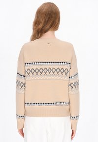 Beżowy sweter robiony na drutach o luźnym kroju, z geometrycznymi wzorami w niebieskim i czarnym kolorze na klatce piersiowej i rękawach. Ribkowane mankiety i dół.