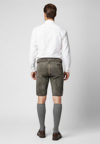 Pantaloni corti in suede grigi con una tasca con zip, indossati con calze grigie al ginocchio e scarpe marroni. Il modello è girato di spalle, mettendo in evidenza il design e la vestibilità.