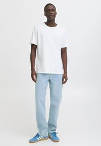 Camiseta de algodón blanca, de corte relajado, combinada con pantalones de denim azul claro. El calzado presenta zapatillas azules con tres rayas blancas.