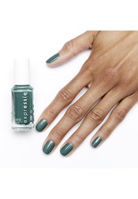 Smalto verde turchese in una bottiglia di vetro trasparente con un tappo bianco, accanto a una mano con unghie curate nello stesso colore.