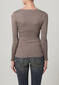 Brązowa prążkowana bluzka z długim rękawem, ozdobiona falistą koronką przy dekolcie i na dole. Dopasowany krój, zestawiona z niebieskimi dżinsami.