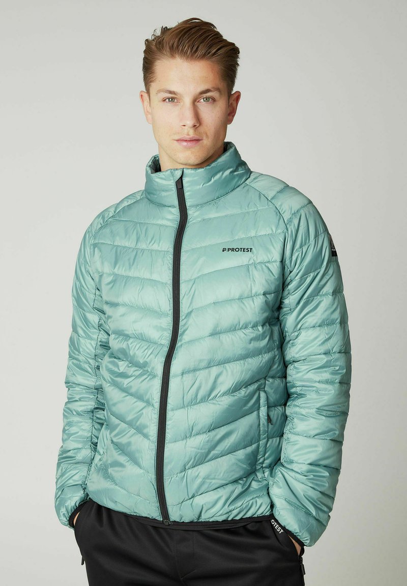 Svijetlo tirkizna puffer jakna napravljena od glatkog, sjajnog materijala. Ima visoki ovratnik i crni patent zatvarač, s dijagonalnim kvalitetom i logotipom.