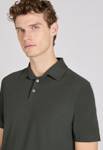 Polo de color verde oscuro hecho de un tejido suave, con cuello y una tapeta de tres botones. Mangas cortas y diseño ajustado.