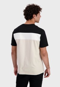 T-shirt a maniche corte con una parte superiore nera e una striscia bianca sul retro, che transita in un segmento inferiore di un beige chiaro.