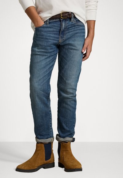 Blå denimjeans med rak passform, lätt distressed finish, uppvikta fållar, i kombination med bruna mocka ankelskor med marinblå accenter.