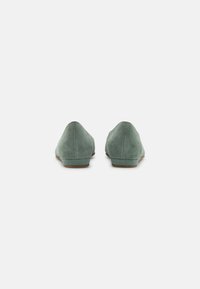 Pantofole in suede verde con un profilo basso, punta arrotondata e texture liscia. La costruzione presenta un design semplice senza hardware visibile.