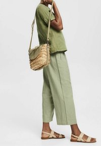 Persona vestida con un conjunto de lino verde claro, sandalias planas beige y llevando un bolso de hombro tejido con tapa y correa de cuero.