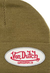 Gorro de punto verde oliva con un parche ovalado blanco que presenta el texto bordado en rojo "Von Dutch ORIGINALS". Textura suave, ajuste ceñido.